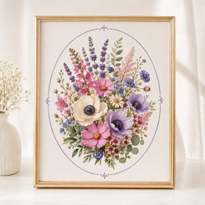 Puede incluir: Una lámina de arte enmarcada con una ilustración en acuarela de un vibrante ramo de flores dentro de un fino borde ovalado de color morado. El ramo incluye anémonas blancas y rosas, lavanda morada, acianos azules y follaje verde.