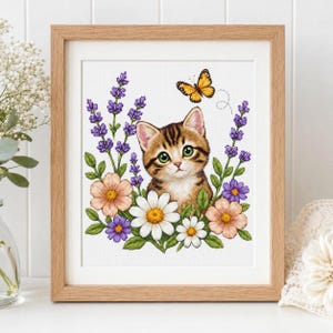 Può includere: Una stampa incorniciata raffigurante un gattino tigrato marrone con occhi verdi circondato da lavanda viola, margherite bianche e fiori color pesca. Una farfalla gialla con segni neri è posizionata sopra la testa del gattino su sfondo bianco.