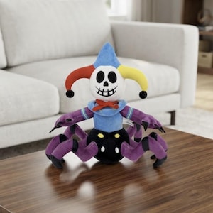 May include: A plush toy featuring a white skull head with a black stitched mouth and eye sockets, wearing a blue, red, and yellow jester hat. The torso is blue with a red neck tie, and the lower body is a black spider-like base with purple legs.