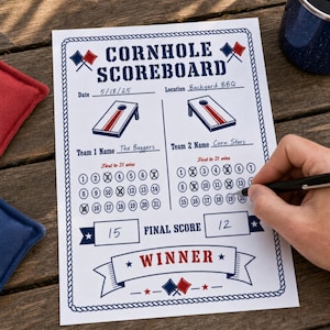 Könnte beinhalten: Ein weißer Cornhole-Spielstandsbogen aus Papier mit blau-roten Grafiken, der Felder für Datum, Ort, Teamnamen und nummerierte Kreise zur Punkteverfolgung bis 21 enthält, sowie einen Bereich für den Endstand und ein Gewinner-Banner am unteren Rand.