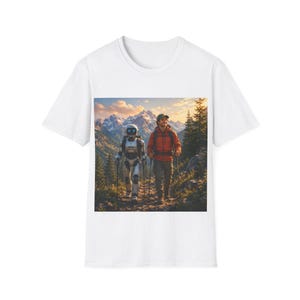 Peut inclure: Un t-shirt blanc avec une impression graphique représentant un randonneur et un robot marchant ensemble sur un sentier de montagne. La scène montre une personne en veste orange et un robot aux yeux bleus lumineux, entourés de pins et de sommets enneigés.