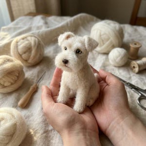 Könnte beinhalten: Eine kleine, cremeweiße, nadelgefilzte Hundefigur mit strukturiertem Wollfell, spitzen Ohren und dunkelbraunen Augen. Die Miniaturskulptur hat eine ausgeprägte Schnauze und eine kleine dunkle Nase und ähnelt einer Terrier-Hunderasse.