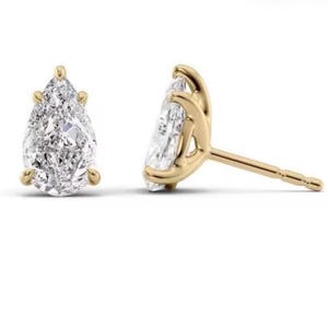 May include: A pair of stud earrings featuring pear-shaped clear gemstones set in yellow gold. One earring is shown from the front, displaying the faceted stone, while the other is shown from the side, revealing the gold prong setting and post.