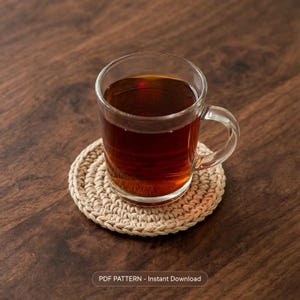 Peut inclure: Une tasse en verre transparent remplie de thé brun foncé posée sur un dessous de verre rond en crochet beige. Le texte en bas de l'image indique : PDF PATTERN - Instant Download.