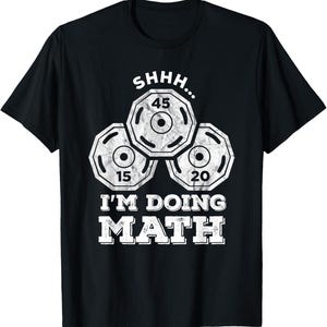 May include: A black short-sleeved t-shirt featuring a white graphic of three weight plates labeled 45, 15, and 20. Above the plates is the text SHHH... and below the plates is the text I'M DOING MATH in a bold, distressed white font.