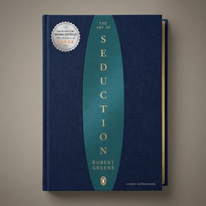 Pode incluir: Um livro de capa dura intitulado The Art of Seduction de Robert Greene com uma capa de tecido azul escuro e um oval central verde-azulado contendo o título em letras douradas. Um selo circular prateado no canto superior esquerdo menciona 48 Laws of Power.