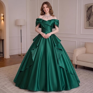 May include: A floor-length emerald green satin gown featuring an off-the-shoulder neckline with draped sleeves, a fitted bodice with subtle pleating, and a voluminous skirt with cascading ruffled layers that extend from the waist to the hem.