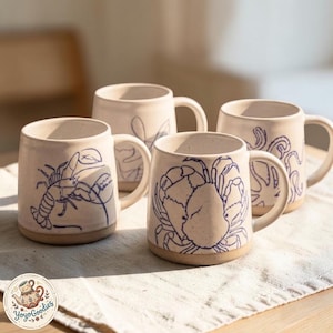 May include: Four off-white ceramic mugs with speckled textures and blue line-art illustrations of sea creatures including a lobster, a crab, and an octopus. Each mug features a sturdy handle and a smooth, unglazed base. A logo reads YoyoGoodies.