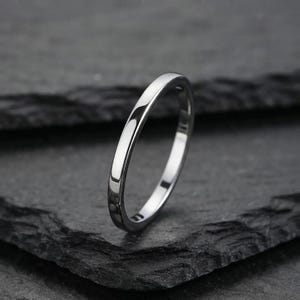 Può includere: Un sottile anello in metallo color argento lucido con una fascia liscia e arrotondata. L'anello presenta un design circolare semplice e continuo con una superficie metallica riflettente che cattura la luce, mostrando un aspetto pulito.