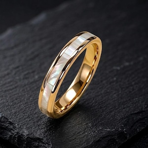 May include: A gold-toned band ring featuring a central inlay of iridescent white mother-of-pearl segments. The ring has a polished, reflective metallic finish and a smooth, rounded profile, showcasing a clean and simple design aesthetic.