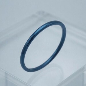 Può includere: Un anello circolare sottile con una finitura liscia e lucida di colore blu marino intenso. La fascia presenta un design semplice e continuo con un profilo arrotondato, mostrando un aspetto metallico uniforme lungo tutta la circonferenza.
