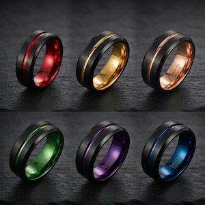 Op de afbeelding: Zes ringen van wolfraamcarbide met een geborstelde zwarte buitenkant en een gepolijste binnenband. De binnenkleuren zijn rood, goud, roségoud, groen, paars en blauw. Elke ring heeft een dunne, bijpassende gekleurde groef in het midden.