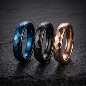 May include: Three rings arranged in a row, each featuring a faceted, diamond-cut geometric pattern. The first ring is a deep metallic blue, the second is a solid black, and the third is a warm rose gold tone, all with a polished, reflective finish.