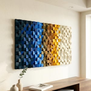 Könnte beinhalten: Ein rechteckiges Wandkunstwerk, das aus zahlreichen kleinen, hervorstehenden Holzblöcken in einem Farbverlauf besteht. Die Farben wechseln von tiefem Marineblau auf der linken Seite über leuchtendes Blau, Gold und Gelb bis hin zu Cremeweiß auf der rechten Seite.