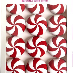 May include: A package of twelve round knobēz decorative knob covers featuring a red and white peppermint swirl pattern. The white box displays the brand name knobēz at the top and the text 12 Pack of Peppermint Knobēz at the bottom.