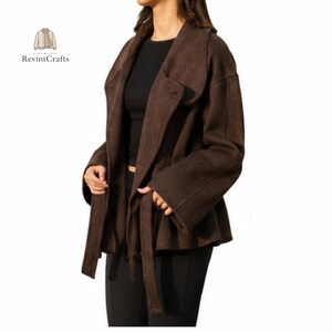 May include: A dark brown jacket with a wide collar, long sleeves, and a matching tie belt at the waist. The jacket is worn over a black top and black trousers. The logo RevintCrafts with a small jacket icon is visible in the upper left corner.