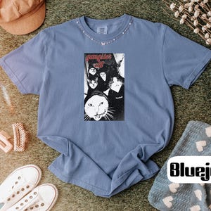 May include: A blue short-sleeve t-shirt featuring a central rectangular graphic print of multiple cats with the text "gangster cat" in red lettering. The shirt has a crew neckline and a relaxed fit, showcasing a vintage-inspired wash.