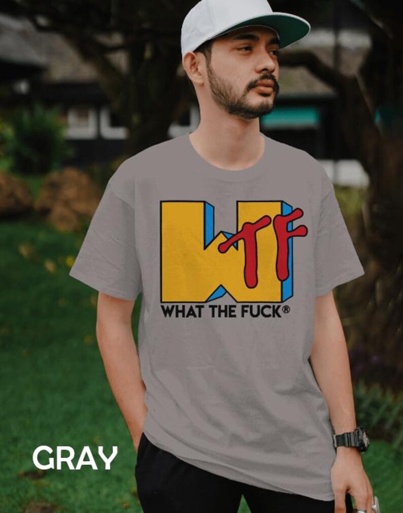 May include: A gray short-sleeved t-shirt featuring a large yellow block letter W with a blue shadow and red stylized TF letters overlapping it. Below the graphic, the text WHAT THE FUCK is printed in black capital letters with a registered symbol.
