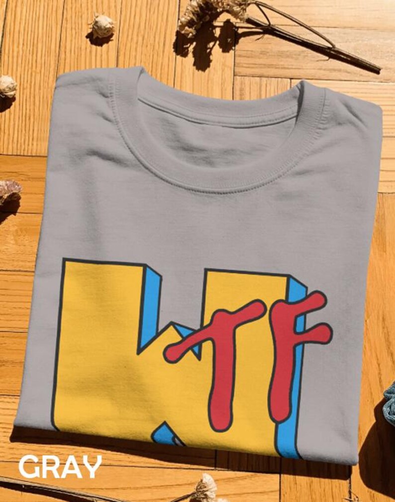 May include: A gray crew neck t-shirt featuring a large graphic print on the front. The design displays the letters KTF in a bold, blocky yellow font with blue 3D-style shading and a red, dripping-style font layered over the yellow letters.