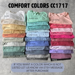 May include: A collection of folded t-shirts in various colors labeled Comfort Colors CC1717. The colors include white, ivory, butter, mustard, yam, sandstone, bay, light green, blue spruce, moss, island reef, chalky mint, seafoam, hydrangea, chambray, blue jean, flo blue, washed denim, denim, gray, pepper, peachy, crunch berry, blossom, watermelon, heliconia, brick, chili, orchid, violet, berry, and black.