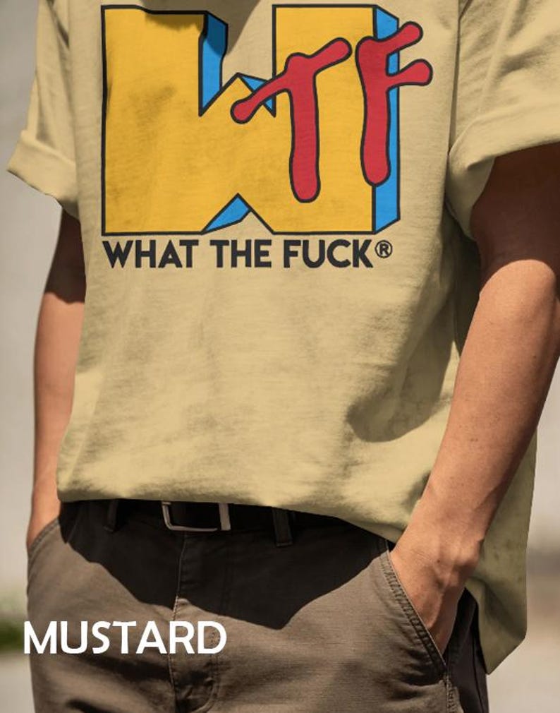 May include: A mustard yellow t-shirt featuring a large graphic print with the yellow block letters WTF, accented by a red script overlay and blue shadows. Below the graphic, the text WHAT THE FUCK is printed in black capital letters.