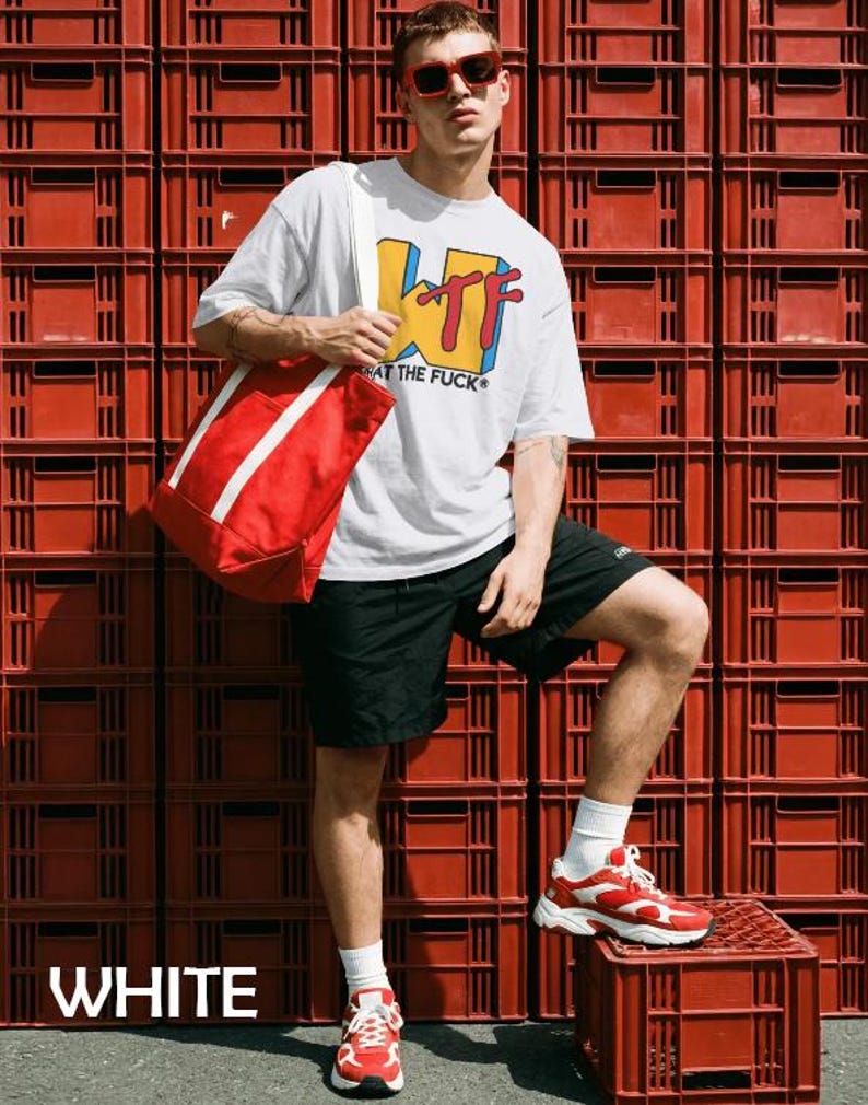 May include: A white short-sleeved t-shirt with a yellow, blue, and red graphic print that reads WTF WHAT THE FUCK, paired with black shorts, a red tote bag with white straps, red-tinted sunglasses, and red and white athletic sneakers with white socks.