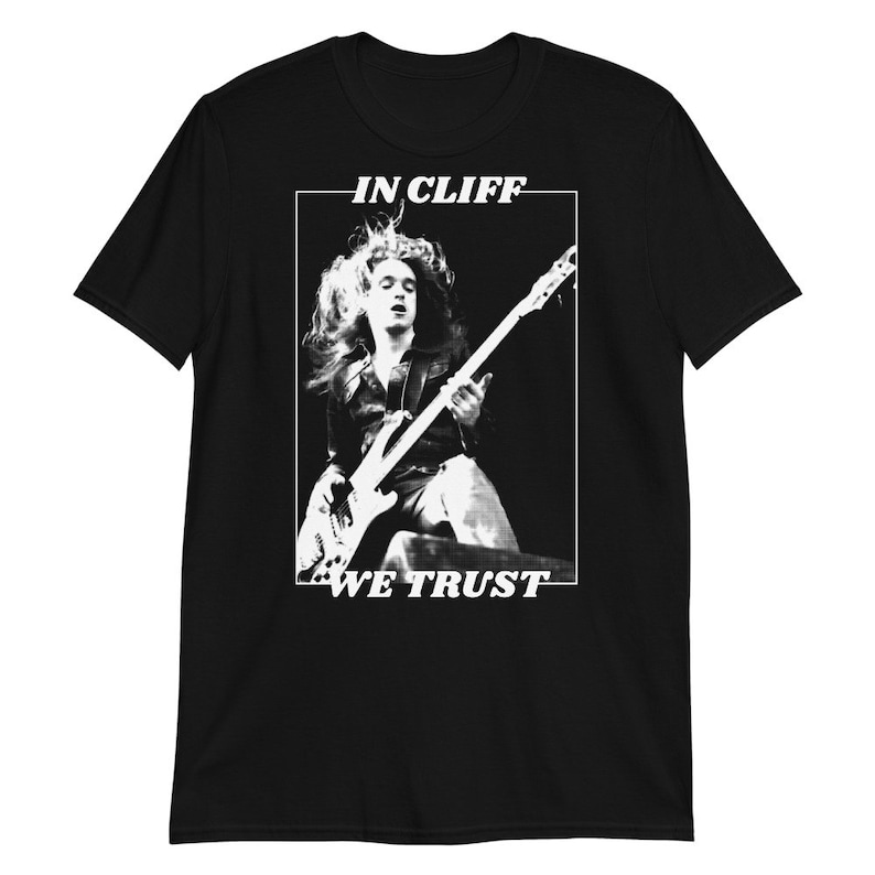 Puede incluir: Imagen en blanco y negro de un m&uacute;sico tocando un bajo. El texto "IN CLIFF WE TRUST" est&aacute; impreso en la camiseta.