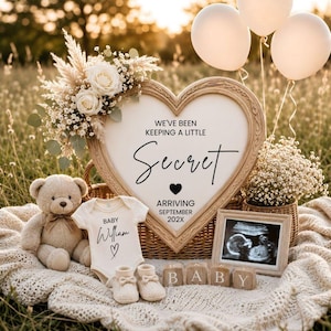 Può includere: Una cornice in legno a forma di cuore con il testo WE'VE BEEN KEEPING A LITTLE Secret ARRIVING SEPTEMBER 202X, un orsacchiotto beige, un body bianco con la scritta BABY William, scarpine color crema, cubi di legno BABY e un'ecografia.