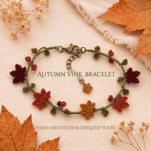 May include: A hand-crocheted bracelet featuring a green vine design adorned with small red, orange, and brown maple leaves and tiny berries. The piece includes a bronze-toned metal lobster clasp and an adjustable chain with a small leaf charm.