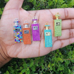 May include: Five silver and gold perfume bottle charms with rhinestones. The charms are decorated with the words "N°1 PARFUM".
