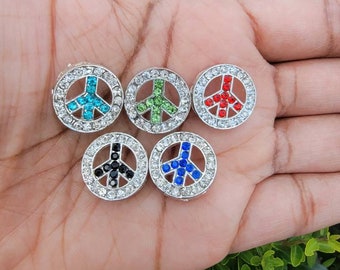 Puede incluir: Seis dijes con forma de signo de paz con diferentes colores de piedras de imitación. Los dijes son plateados con un borde de piedras de imitación blancas. Los colores de las piedras de imitación son azul, verde, rojo, negro, azul y rojo.