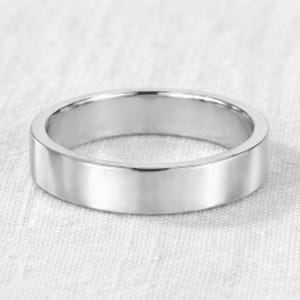 Puede incluir: Un anillo de metal plateado pulido con una superficie lisa y plana y un diseño de banda simple y continuo. El anillo presenta un acabado reflectante y un ancho uniforme en todo su contorno, mostrando una estética limpia y sin adornos ni grabados.