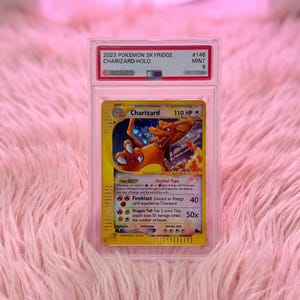 Könnte beinhalten: Eine bewertete 2023 Pokemon Skyridge Charizard-Holo Sammelkarte in einer durchsichtigen Kunststoff-Schutzhülle. Die Karte hat einen gelben Rand, eine holografische Illustration des orangefarbenen Charizard-Charakters und Text.