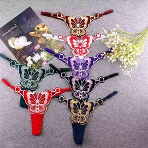Peut inclure: Une collection de six strings, chacun orné d'un motif de papillon brodé sur le devant. Les papillons sont déclinés en plusieurs couleurs, notamment rouge, blanc, violet, noir, vert et doré, avec des lanières assorties pour chaque pièce.