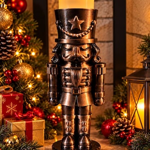 May include: A bronze-coloured nutcracker figurine standing on a circular base, featuring a tall hat with a star emblem and a rope detail. The top of the nutcracker holds a cylindrical, glowing yellow LED candle that emits a warm light.