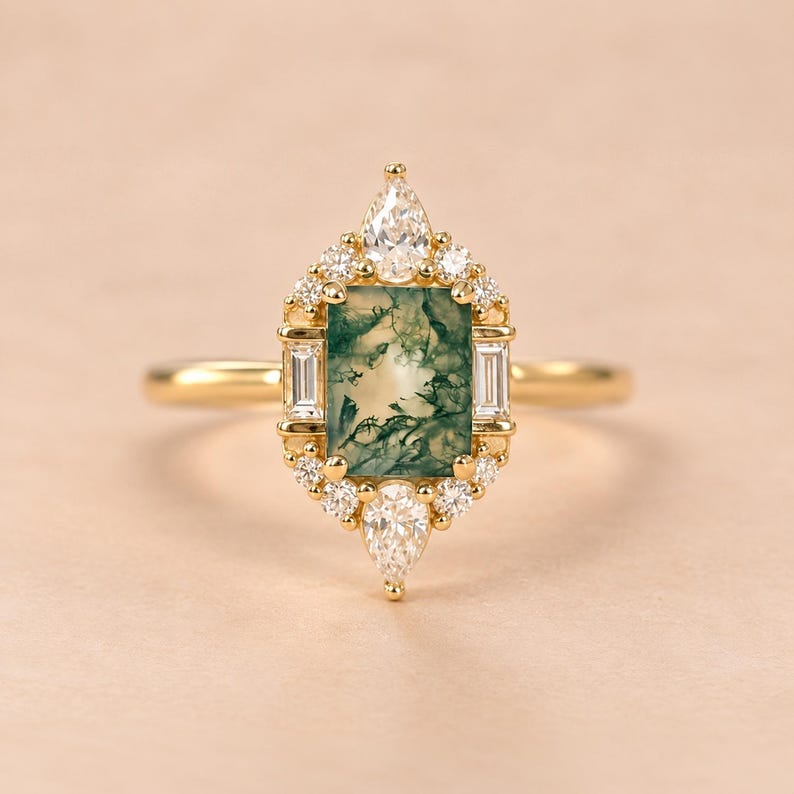 May include: A gold ring featuring a rectangular moss agate centre stone with green inclusions. The stone is surrounded by a halo of small round and baguette-cut white diamonds, with a pear-shaped diamond at the top and bottom of the setting.