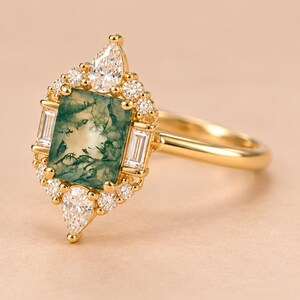 May include: A gold ring featuring a rectangular moss agate centre stone with green inclusions. The stone is surrounded by a halo of small round diamonds, two baguette-cut diamonds on the sides, and two pear-shaped diamonds at the top and bottom.