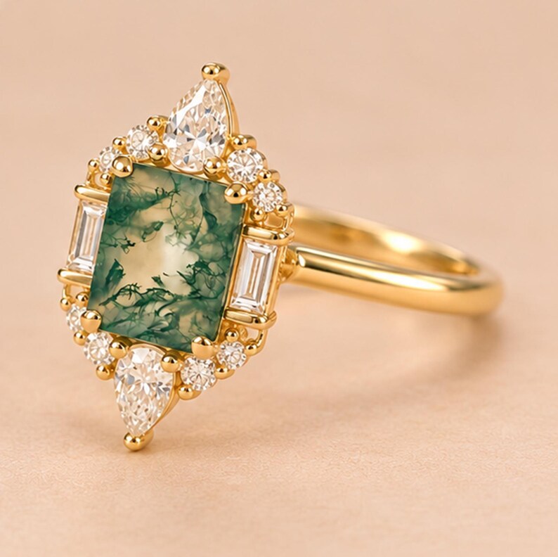 May include: A gold ring featuring a rectangular moss agate centre stone with green inclusions. The stone is surrounded by a halo of small round diamonds, two baguette-cut diamonds on the sides, and two pear-shaped diamonds at the top and bottom.