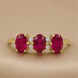 Puede incluir: Un anillo de oro con tres rub&iacute;es de color rojo intenso en talla oval dispuestos horizontalmente. Los rub&iacute;es est&aacute;n separados por peque&ntilde;os diamantes blancos redondos y claros engastados en oro. La banda es de oro amarillo pulido con dise&ntilde;o cl&aacute;sico.