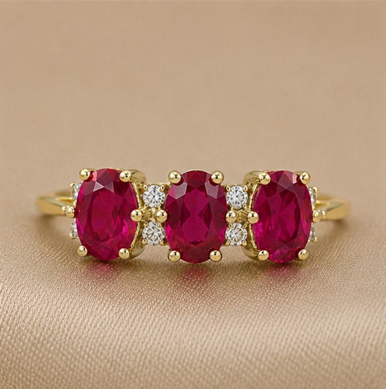 Puede incluir: Un anillo de oro con tres rub&iacute;es de color rojo intenso en talla oval dispuestos horizontalmente. Los rub&iacute;es est&aacute;n separados por peque&ntilde;os diamantes blancos redondos y claros engastados en oro. La banda es de oro amarillo pulido con dise&ntilde;o cl&aacute;sico.