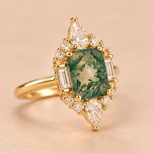 May include: A gold ring featuring a rectangular moss agate centre stone with green inclusions. The stone is surrounded by a halo of small round diamonds, two baguette-cut diamonds on the sides, and two pear-shaped diamonds at the top and bottom.