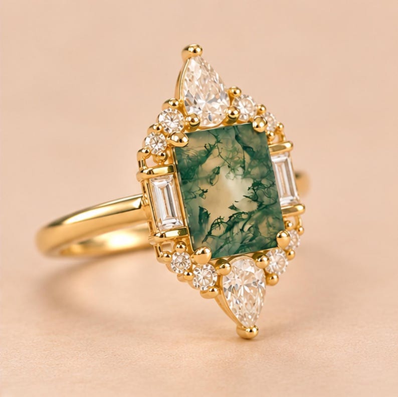 May include: A gold ring featuring a rectangular moss agate centre stone with green inclusions. The stone is surrounded by a halo of small round diamonds, two baguette-cut diamonds on the sides, and two pear-shaped diamonds at the top and bottom.