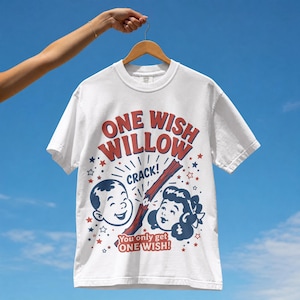 Könnte beinhalten: Ein weißes Kurzarm-T-Shirt mit einem Grafikdruck, der den Text ONE WISH WILLOW, CRACK! und You only get ONE WISH! zeigt. Das Design enthält Illustrationen von zwei Gesichtern, einem zerbrochenen braunen Stock sowie kleinen roten und blauen Sternen.