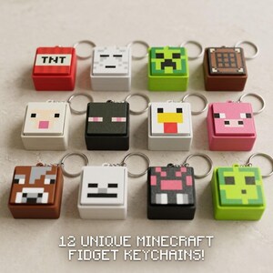 Puede incluir: Una colección de doce llaveros fidget cuadrados con diseños pixelados inspirados en personajes y objetos de Minecraft, incluyendo TNT, un Creeper, una mesa de trabajo, una oveja, un Enderman, un pollo, un cerdo, una vaca, un esqueleto y un slime.