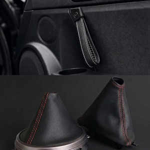 Può includere: Una maniglia a cinghia in pelle nera con cuciture bianche montata su un pannello portiera, insieme a due cuffie per leva del cambio in pelle nera con cuciture rosse, presentate come componenti di ricambio per auto.