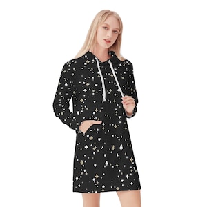 May include: A black hooded sweatshirt dress featuring a repeating pattern of white playing card suits including hearts, diamonds, clubs, and spades, interspersed with small gold and white four-pointed star shapes. The garment has long sleeves and white drawstrings.