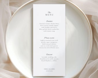Pode incluir: Um cartão de menu retangular branco com texto preto centralizado num prato redondo branco. O menu lista Starters, Main course e Dessert, incluindo pratos como toasted coconut chicken bites, truta e bolo de casamento de lavanda, terminando com Emma & James 28.08.2027.