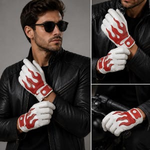 May include: A pair of white leather gloves featuring a bold red flame pattern across the back of the hand. The gloves include a wrist strap with a white snap button closure, providing a secure fit. The design is consistent across both hands.