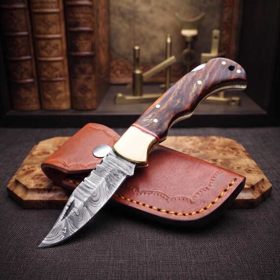 Hand-forged Damascus steel folding knife with a rosewood handle and leather sheath — the layered Damascus pattern alone makes this a genuine conversation piece.