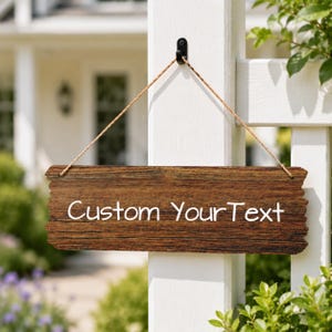 May include: A rectangular wooden sign with a dark brown wood grain finish, featuring the white text Custom YourText. The sign has rough, uneven edges and is suspended by a thin, light brown twine rope from a black metal hook on a white post.